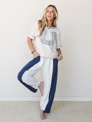 A relaxed, full-body shot of a model in a cream graphic tee and wide-leg color-block pants — cream with navy side panels — styled with stacked turquoise and beaded bracelets for an effortlessly put-together, cozy-cool vibe.