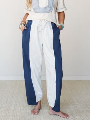 A relaxed pair of color-block barrel pants in heathered grey and navy with a front center stripe panel, styled with a cream embroidered top and stacked turquoise bracelets — easy, expressive, and very much the kind of thing you'd wear barefoot all da