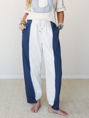 A relaxed pair of color-block barrel pants in heathered grey and navy with a front center stripe panel, styled with a cream embroidered top and stacked turquoise bracelets — easy, expressive, and very much the kind of thing you'd wear barefoot all da