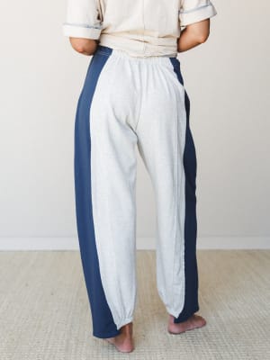 Shot from the back, a model wears relaxed colorblock barrel pants with a heathered grey center panel and navy side panels, paired with a cream short-sleeve top — effortless and cozy with a retro-sporty undertone.
