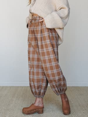 A relaxed, earthy outfit pairing voluminous plaid pants in warm latte tones with a chunky cream knit sweater and brown clogs — the kind of put-together-but-comfortable look that makes a Tuesday feel intentional.