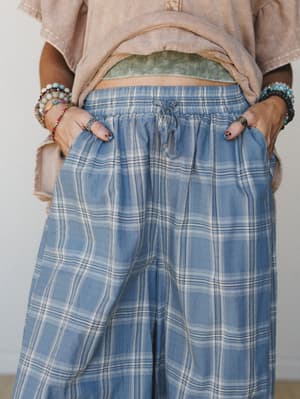 A close-up mid-shot of wide-leg plaid pants in a faded steel blue, styled with a cropped washed tee and layered beaded bracelets — the kind of outfit that looks effortless but was absolutely thought about.