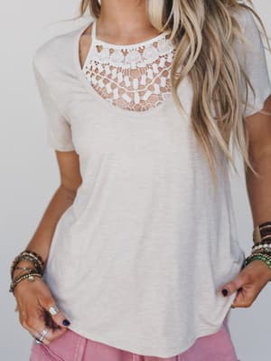 A woman wears a beige short-sleeved tee with the Crochet High Neck Bralette in Ivory peeking from the neckline, pink shorts, and layered bracelets. Her long blonde hair flows loose as she poses with one hand in her pocket.