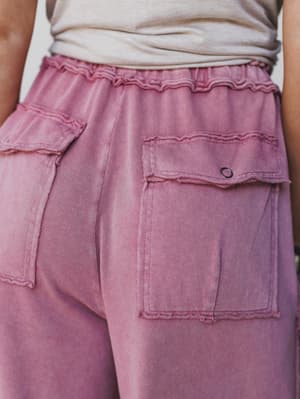 Close-up of a person wearing the Game On Cargo Wide Leg Pant in burgundy, featuring large frayed patch pockets, a drawstring stretch waist, and an elastic waistband. Styled with a light beige top for a comfy boho look.