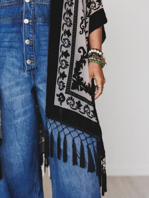 A person wearing high-waisted blue jeans with buttons, the Crushin' On You Velvet Kimono - Black, multiple beaded bracelets, and rings stands against a neutral background.