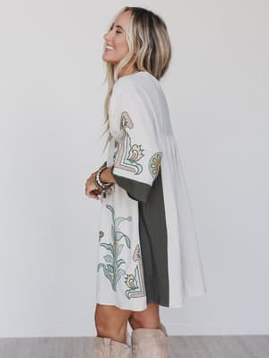 side view of woman wearing caftan style dress in cream with print accents and gray trim