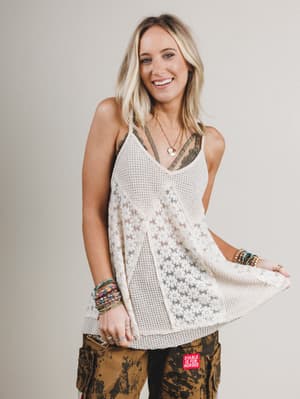 Woman wearing a white lace top and patterned pants on a plain background