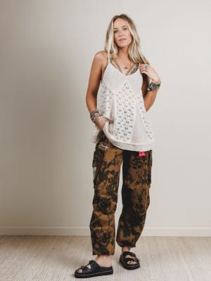 Woman wearing a white lace top and camouflage pants against a plain background
