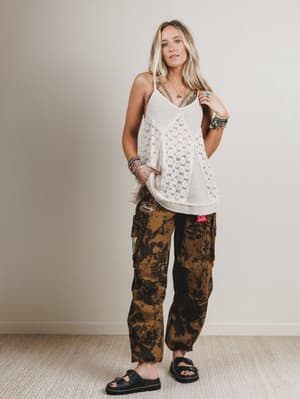 Woman wearing a white lace top and camouflage pants against a plain background