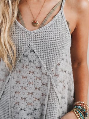 Close-up of a woman wearing a gray patterned tank top over a bralette and wearing several boho bracelets.