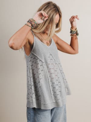 Woman wearing a sleeveless textured top and light blue jeans against a plain background