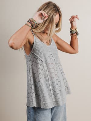 Woman wearing a sleeveless textured top and light blue jeans against a plain background