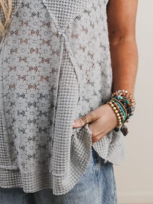 Close-up of woman wearing a textured gray sleeveless top with denim jeans and several boho bracelets.
