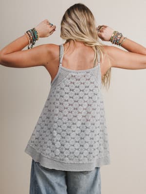 Back view of woman wearing a light gray patterned tank top and blue jeans against a beige background