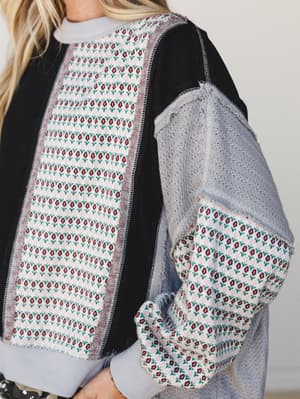 A close-up detail shot of a mixed-fabric top that feels like it was stitched together from a very good thrift haul — patchwork panels of floral jacquard, open-knit grey fabric, and solid black come together in a way that's intentionally imperfect and