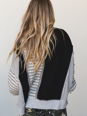 A back-facing shot of a mixed-media cropped top layered over camo pants — black patchwork panels meet a ditsy floral print and lavender knit sleeves for a look that feels like it was assembled with intention and a good playlist.