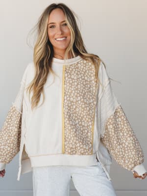 A mixed-media pullover top in cream and tan with daisy floral panels, worn with light grey joggers — the kind of top that makes a Sunday errand run feel like a whole moment.