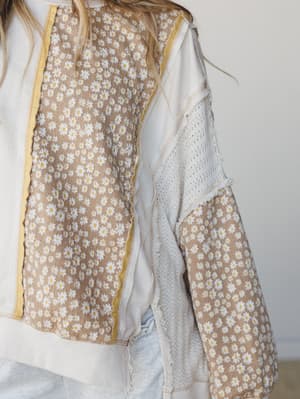 A close-up detail shot of a mixed-fabric pullover top combining daisy print panels, waffle knit, and lace inserts — the kind of piece that looks like it was made from your favorite things all at once.