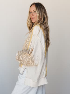 A relaxed, lived-in pullover top in cream with mixed fabric panels — pointelle knit sleeves, daisy-print floral panels, and yellow contrast stitching — styled with light grey sweats and a matching daisy-print bag for an effortlessly cozy, put-togethe