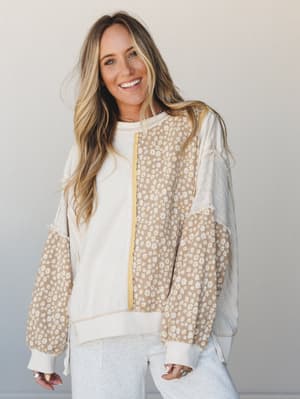 A mixed-media pullover top in cream and tan with daisy print panels, pointelle lace sleeves, and exposed seam detailing — the kind of top that feels like a lazy Sunday but looks like you tried.
