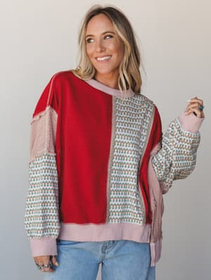 A mixed-fabric pullover top in bold scarlet red and a ditsy floral print, styled with light wash jeans — the kind of top that looks like it was made from your favorite things all at once.