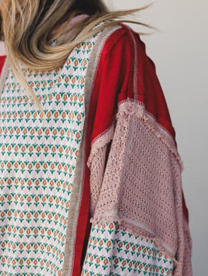 A close-up back shot layering a printed floral jacquard panel, a red thermal waffle-knit layer, and a blush open-knit sleeve — the kind of thoughtful mixed-fabric detail you notice when someone walks past you.