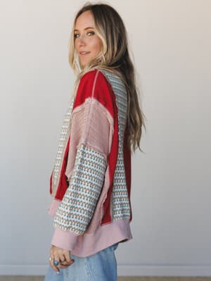 A patchwork mixed-fabric top in scarlet red, dusty pink, and floral-printed knit panels shot in profile — the kind of piece that looks like it was made from your favorite things all at once.