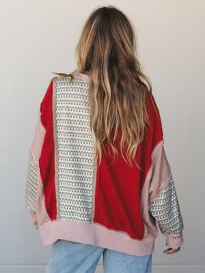 Shot from the back, this patchwork pullover top mixes a bold scarlet red knit panel with a cream floral print and blush lace-textured sleeves — the kind of piece that looks like it was made from your favorite things all at once.