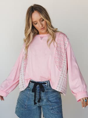 A relaxed, oversized pink long-sleeve top with floral patchwork panels along the sides and sleeves, paired with wide-leg denim — the kind of effortless outfit that looks like you put it together in five minutes but actually has a lot going on.
