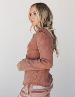 A side-profile shot of a model in a washed ribbed cropped top in a warm chocolate rust tone, paired with a multicolor striped bottom — relaxed, lived-in, and effortlessly put-together.