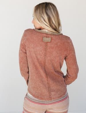 Shot from the back, this acid-washed ribbed long-sleeve top in a warm chocolate rust has the kind of lived-in character that feels intentional — a center back seam with decorative stitching, contrast raw-edge collar, and a woven patch detail make it
