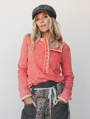 A lived-in, effortlessly cool outfit pairing a washed coral henley thermal top with paisley patchwork pants and a charcoal baker boy cap — the kind of put-together-but-not-trying look that feels like a Saturday with nowhere to be.