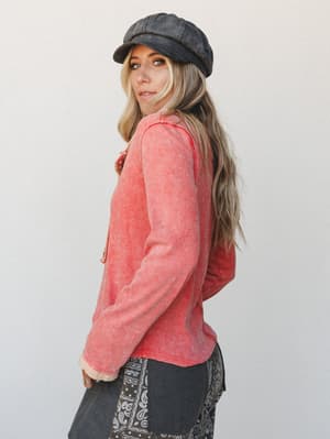 A model shot from the side showing a washed coral waffle-knit long sleeve top paired with charcoal paisley wide-leg pants and a baker boy cap — the whole look reads effortlessly lived-in, like she grabbed it off the chair and made it work.