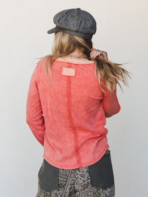 Shot from behind, a model in a washed coral thermal top and paisley patchwork pants fixes her hair — effortlessly lived-in and expressive, like a Sunday that stretched into something worth remembering.