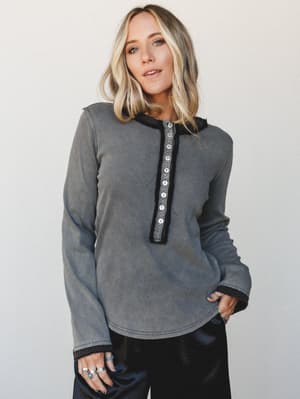 A washed grey ribbed henley top with contrast button placket and cozy knit trim, styled with black satin wide-leg pants — relaxed and a little lived-in, in the best way.