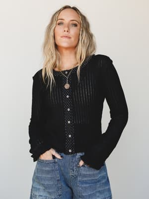 A relaxed layered look featuring a black open-front cardigan worn over a polka dot button-up top, paired with light wash jeans — effortlessly put-together with a lived-in, everyday ease.