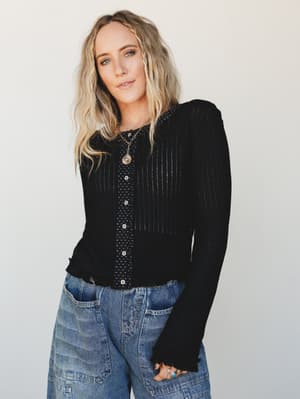A black ribbed cardigan layered over a dotted button-front top, paired with wide-leg cargo jeans and stacked boho jewelry — the kind of effortless layering combo that looks like you figured it out on purpose.