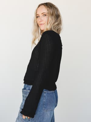 A side-profile studio shot of a black ribbed cardigan paired with medium-wash jeans — the kind of effortless layering piece that looks equally at home on a coffee run or a casual night out.