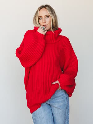 An oversized ruby red chunky knit turtleneck sweater styled with light wash jeans — the kind of sweater that makes you look like you're having a great winter on purpose.