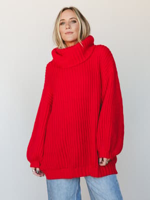 A chunky red turtleneck sweater worn oversized and long over wide-leg light wash jeans — the kind of piece that makes staying in feel just as intentional as going out.