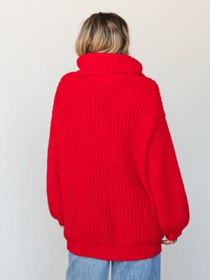 A back-view shot of a bold ruby red chunky turtleneck sweater styled with wide-leg jeans — the kind of cozy, statement piece that makes you want to grab coffee and walk somewhere slowly.