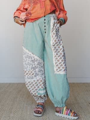 Patchwork wide-leg pants in mint stripe, floral, and lace panels styled with a cropped coral top, stacked bracelets, and rainbow platform sandals — the kind of outfit that has a whole personality.