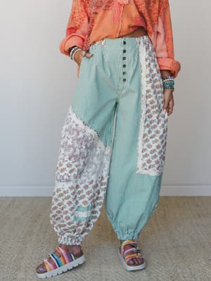 A patchwork harem-style pant in teal stripe, ditsy floral, and sheer lace panels styled with a coral printed top and rainbow platform sandals — playful, collected, and very much its own thing.