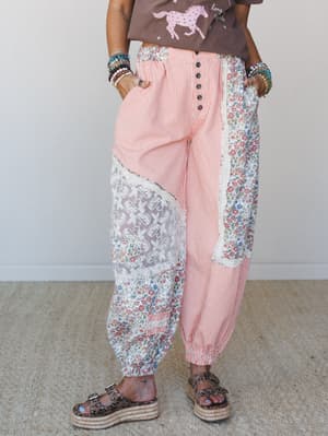 Patchwork harem-style pants in coral stripe mixed with floral and lace panels, styled with a graphic tee, stacked bead bracelets, and platform sandals — the kind of pants that have a whole personality before you even put them on.