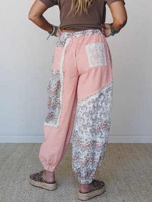 A back-view shot of patchwork jogger pants in coral stripe, floral, and lace panels styled with a brown tee and platform espadrilles — the kind of pants that make you feel like you found them at a market in another country.