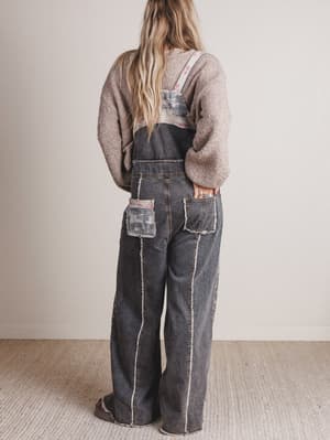 Person wearing denim overalls with a neutral background
