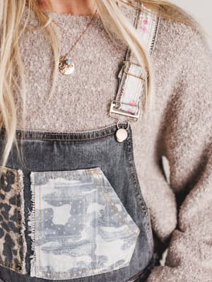 Person wearing a textured sweater and denim overalls with a leopard print pocket.