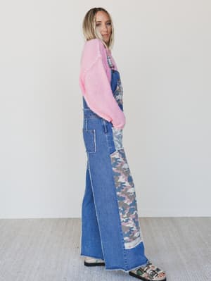 Person wearing a pink sweater and blue overalls with camouflage pattern on a white background