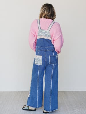 Person wearing a pink sweater and blue denim overalls with floral patterns on a white background