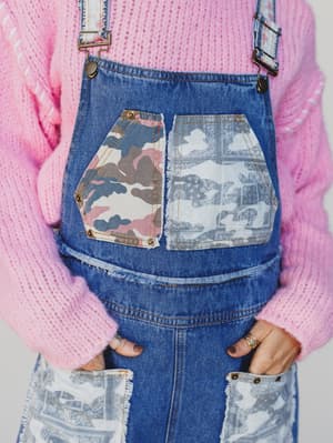 Person wearing blue denim overalls with patchwork design, pink sweater, and floral patterned suspenders.